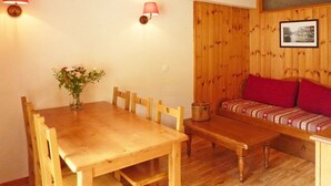 Ein Holztisch mit Stühlen, eine kleine Vase mit Blumen und eine Holzbank mit roten Kissen.
