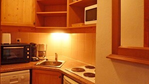 Eine kompakte Küche mit Holzschränken, einer Mikrowelle, einer Kaffeemaschine, einem Geschirrspüler und einem Herd.