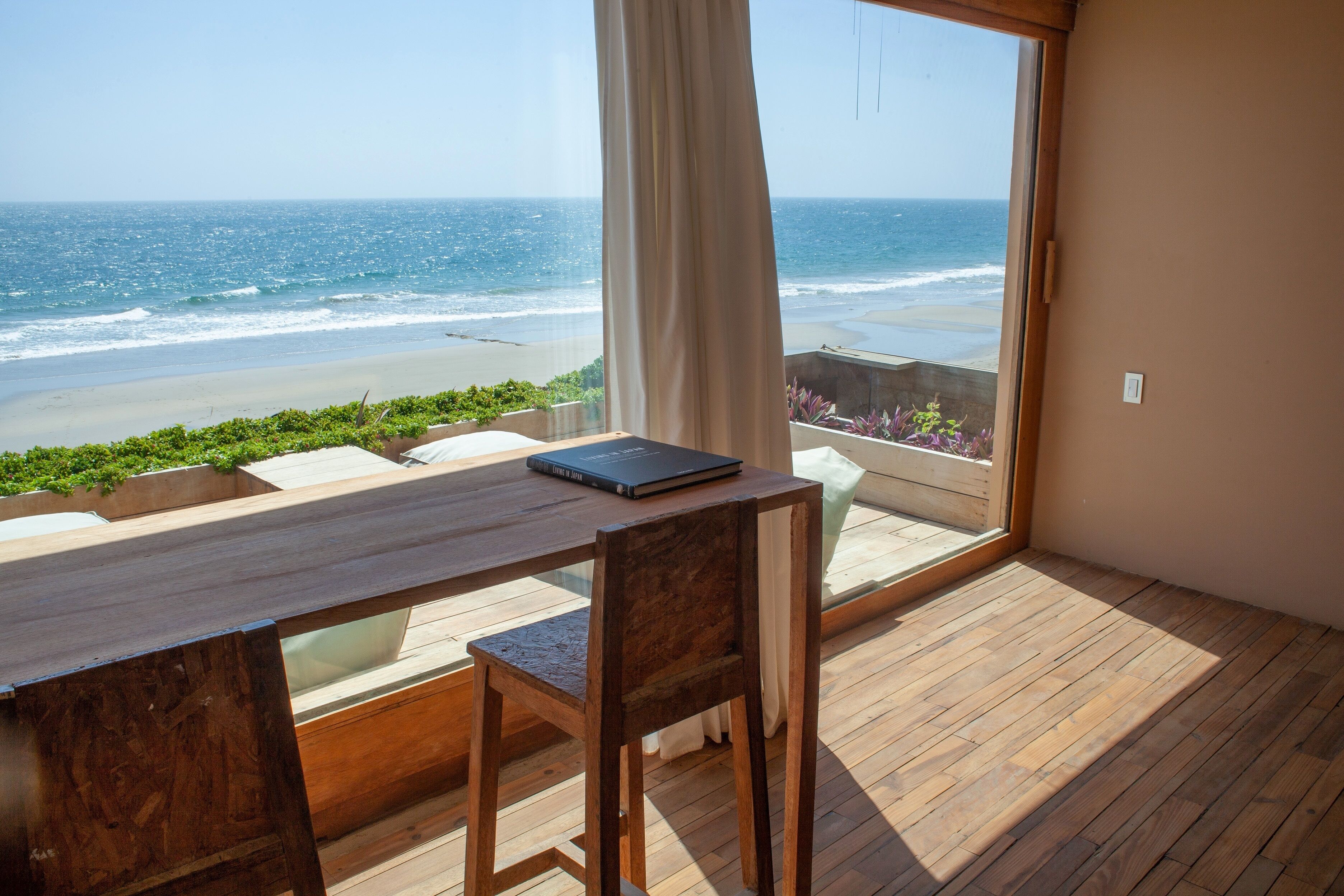 Una terraza de madera con una mesa y una silla, con vistas a una playa y al océano.