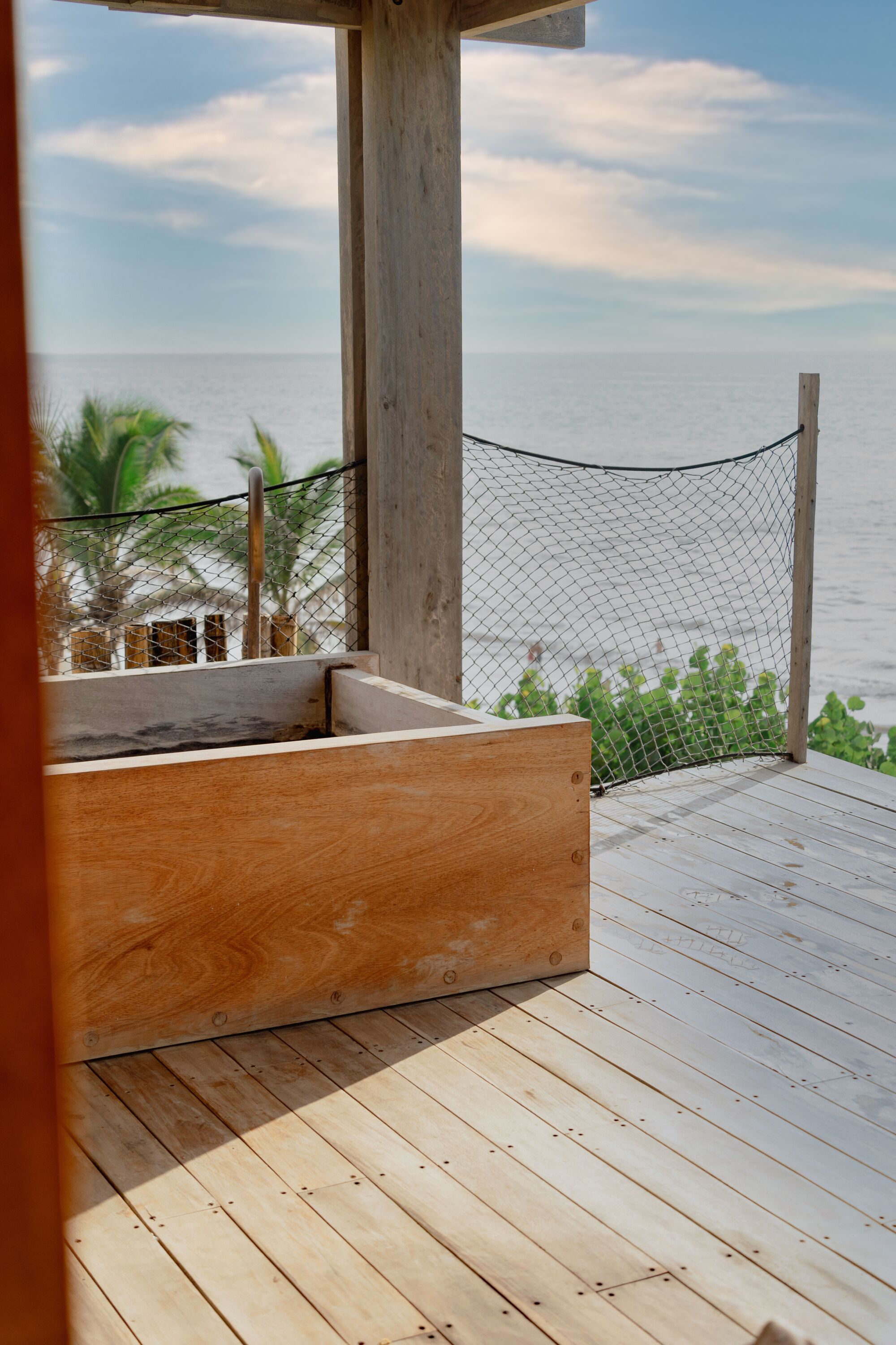 A wooden deck with a wooden bench, a rope barrier, and a view of the ocean.