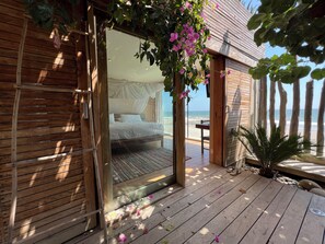 Terraza de madera con una cama y vista a la playa.