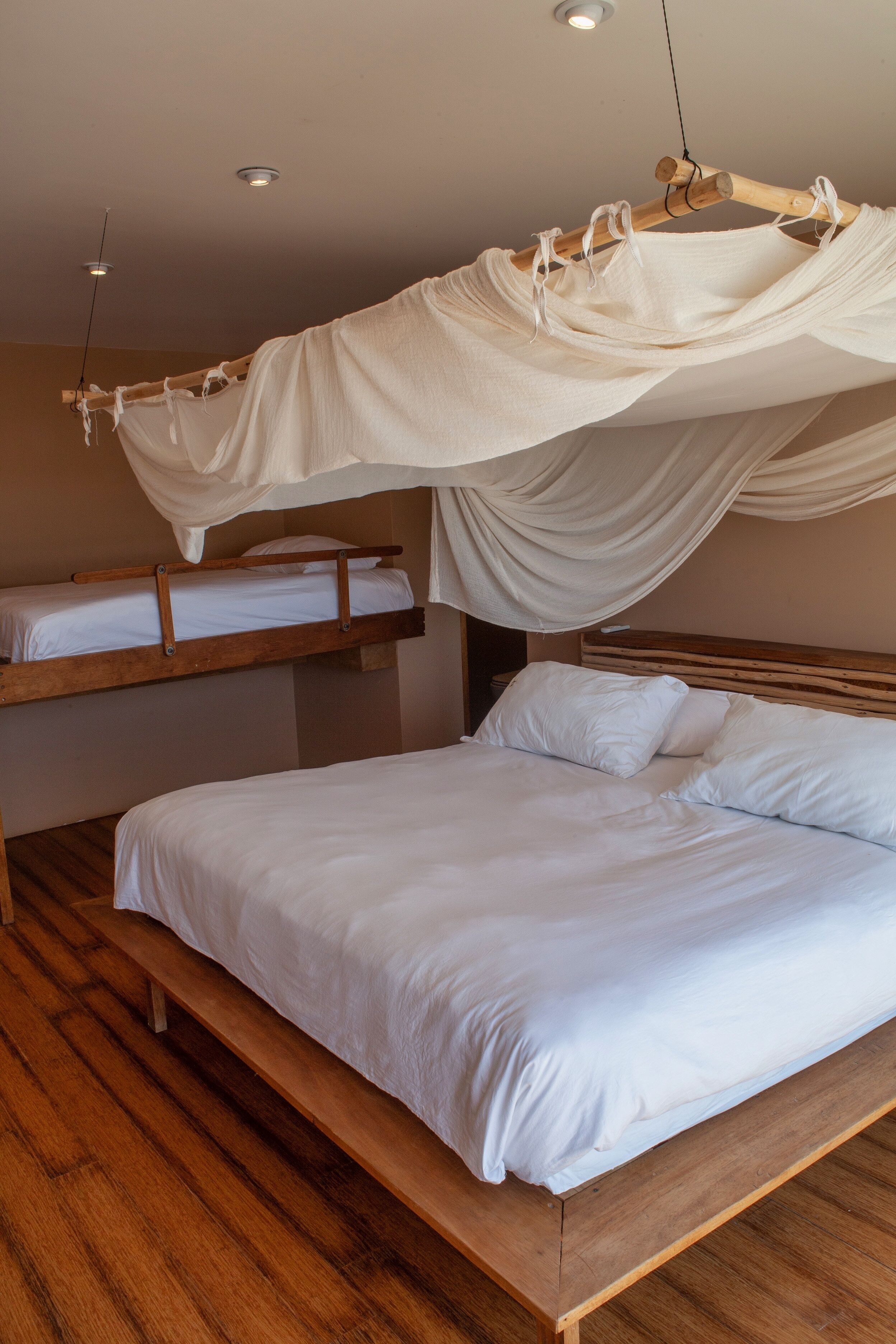 A room with a large bed, a smaller bunk bed, wooden flooring, and a canopy bed.