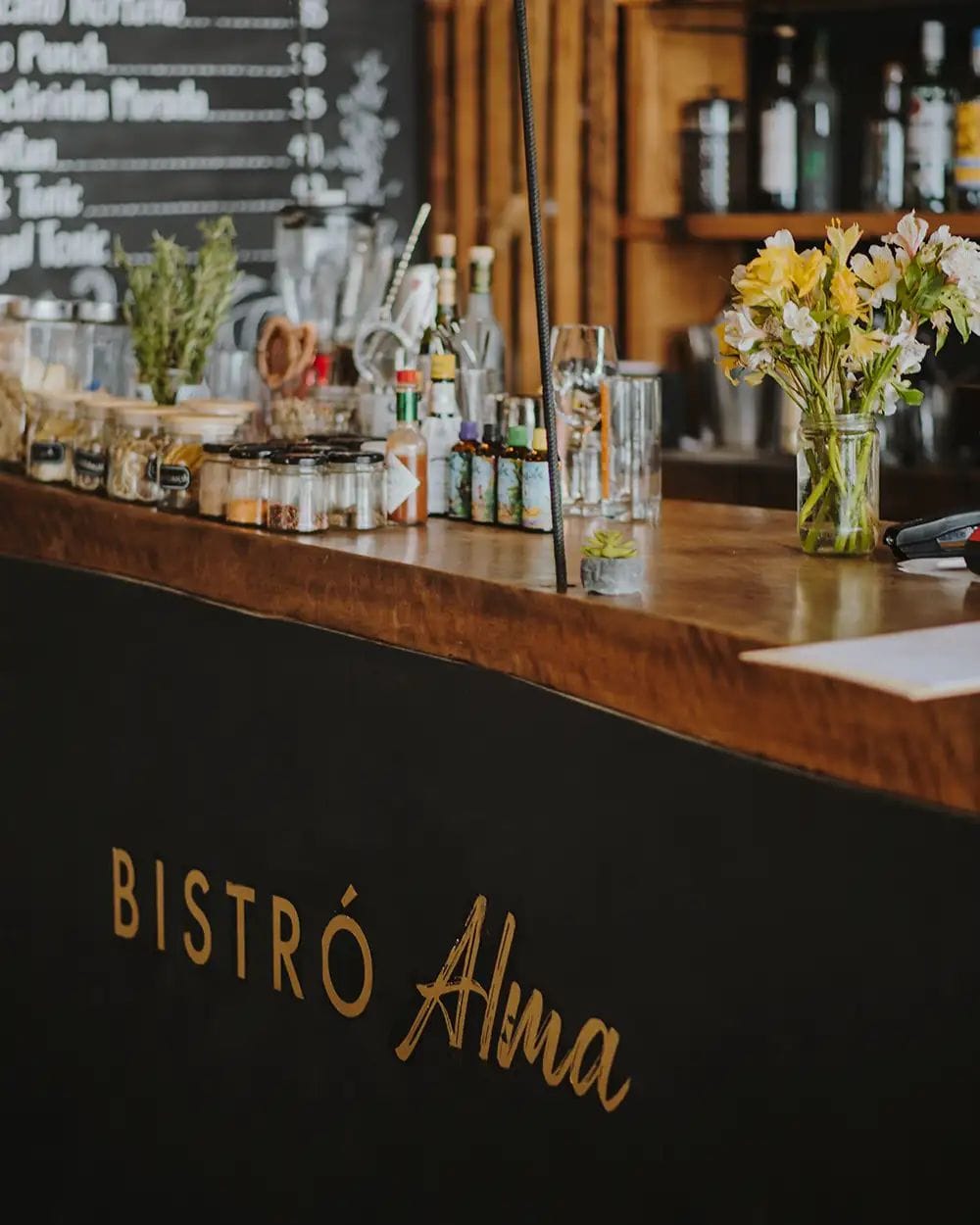 A bar counter with a blackboard menu and various bottles and jars.