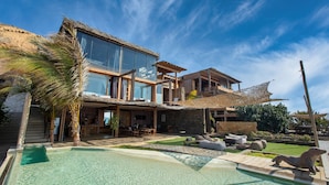 Una casa moderna con piscina, mobiliario exterior y una estructura de techo de paja.