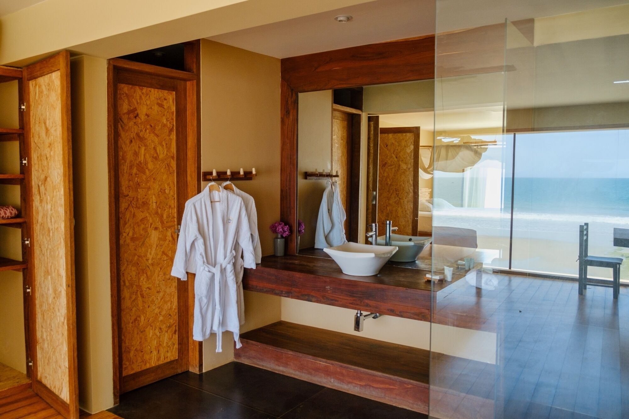 A modern bathroom with a large mirror, wooden vanity, and a view of the ocean.