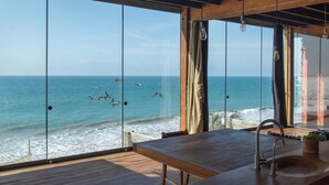 Una terraza de madera con área de cocina y grandes ventanales con vista al océano.