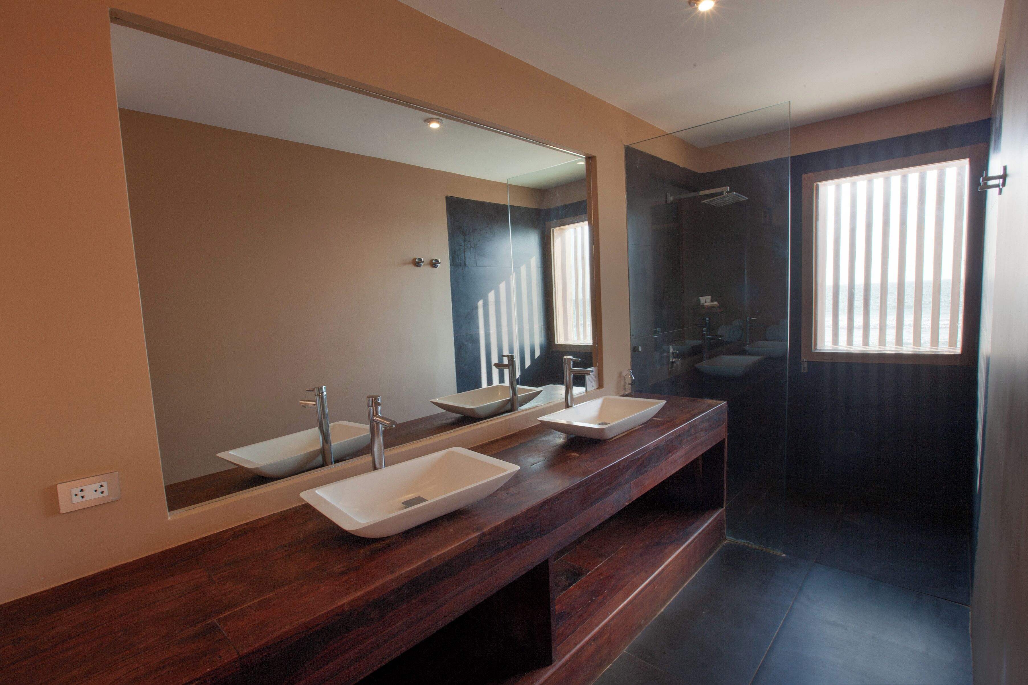A modern bathroom with three sinks, a large mirror, and a glass-enclosed shower.
