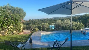 Une piscine offrant une vue sur un paysage vallonné, entourée de verdure et agrémentée d’une pergola.