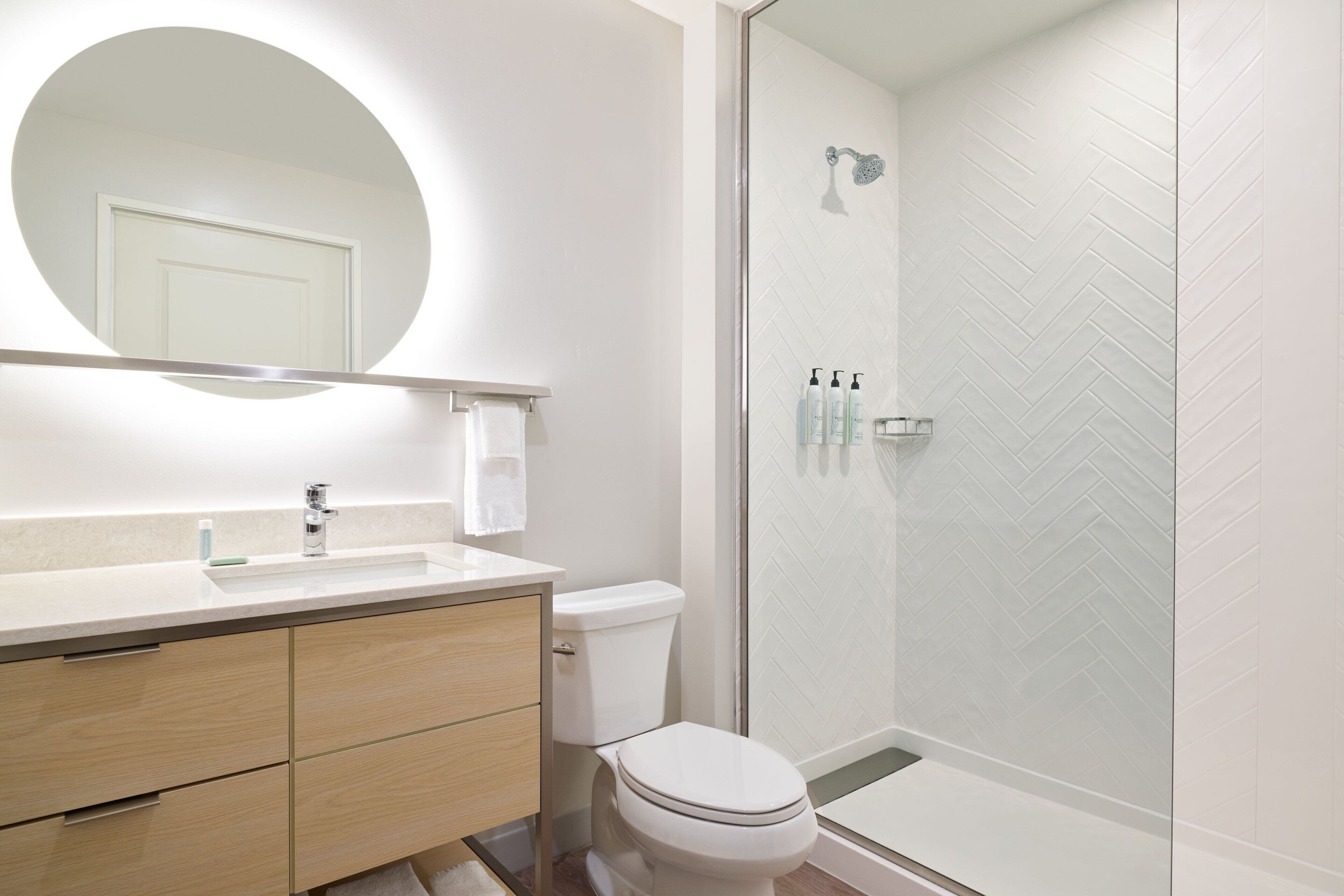 Un baño moderno con un espejo redondo, un lavamanos, un inodoro y una ducha con mampara de vidrio.