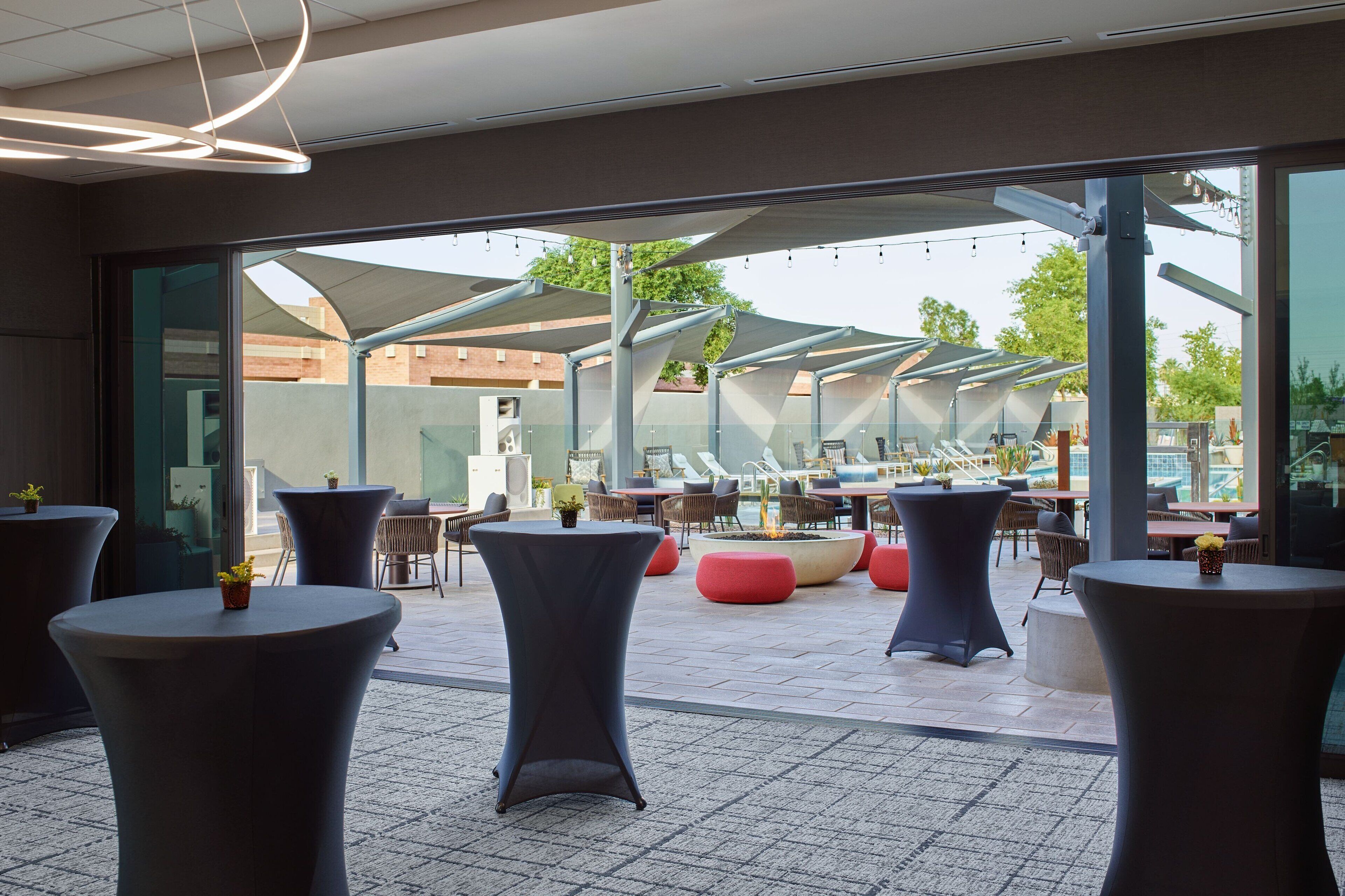 A modern outdoor seating area with round tables and chairs, large windows, and a view of the cityscape.