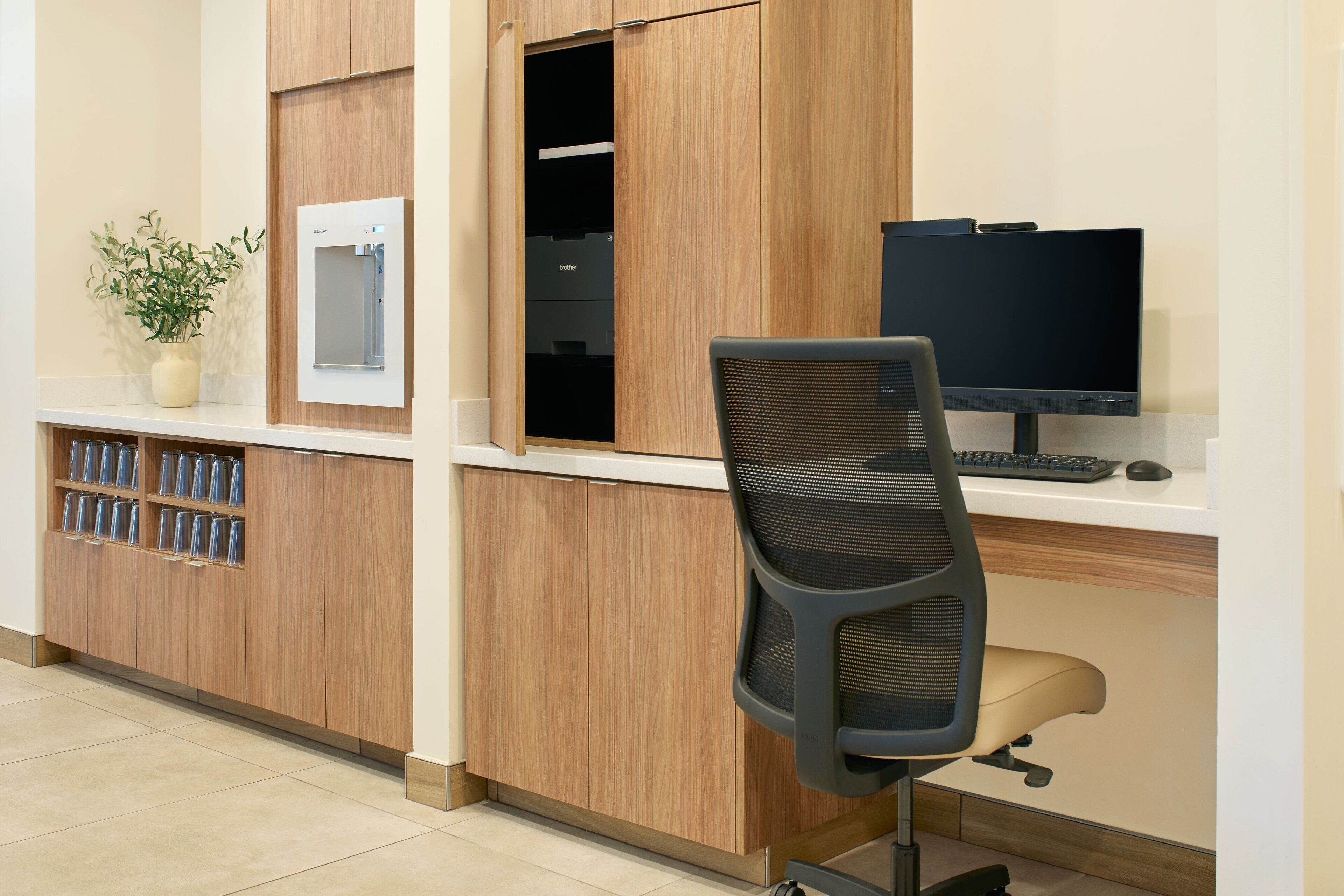 A reception desk with a computer monitor, a keyboard, and a mouse. There is a chair in front of the desk. A potted plant is on the counter.