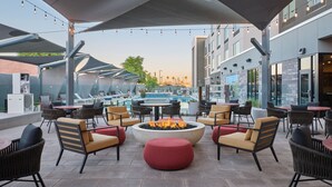 An outdoor seating area with a fire pit, lounge chairs, and tables, overlooking a pool and buildings. - Towneplace Suites By Marriott Tempe (Tempe)
