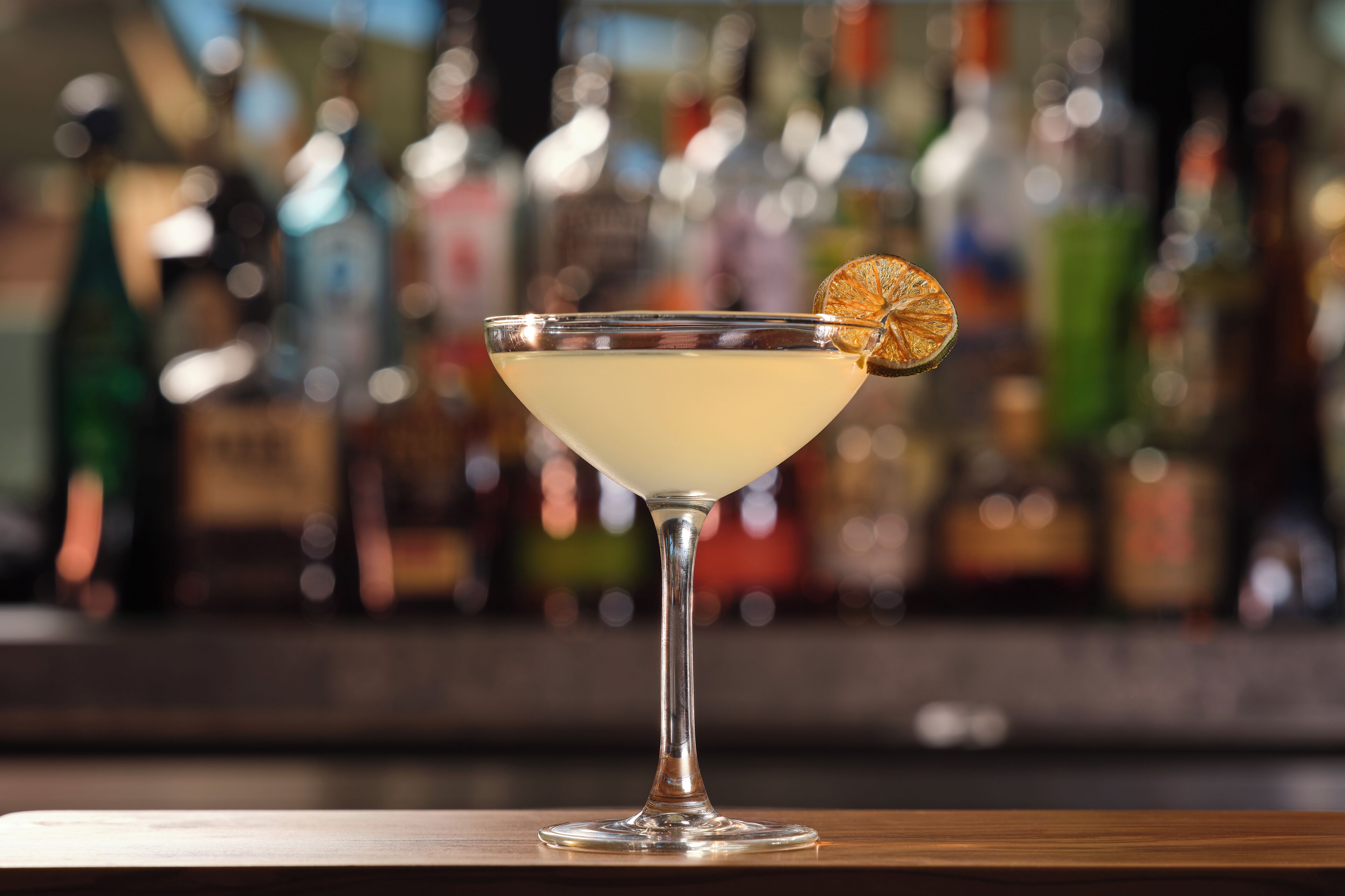 A cocktail in a martini glass with a lemon twist garnish on a bar counter.