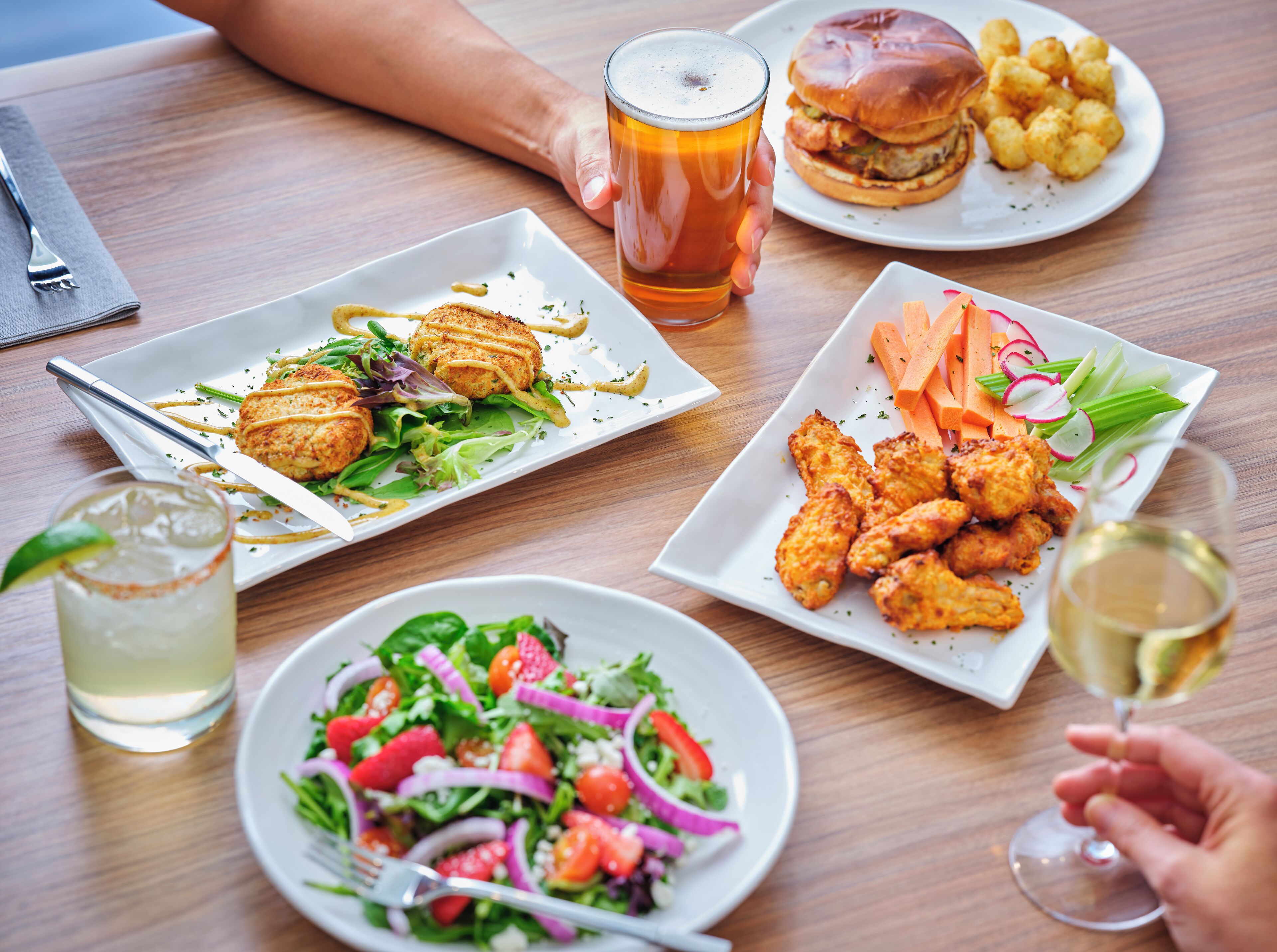 Una mesa de comedor con varios platos, incluyendo una hamburguesa, alitas de pollo y una ensalada.