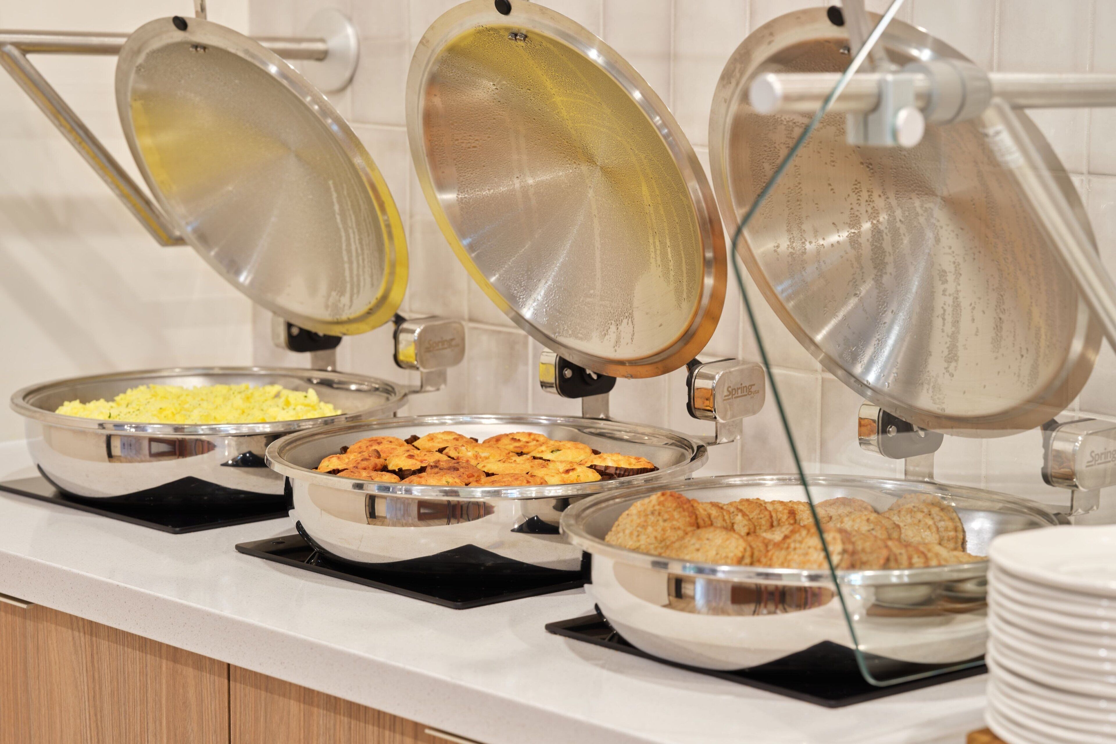 Een buffetopstelling met diverse etenswaren in metalen serveerschaaltjes, afgedekt met glazen deksels.