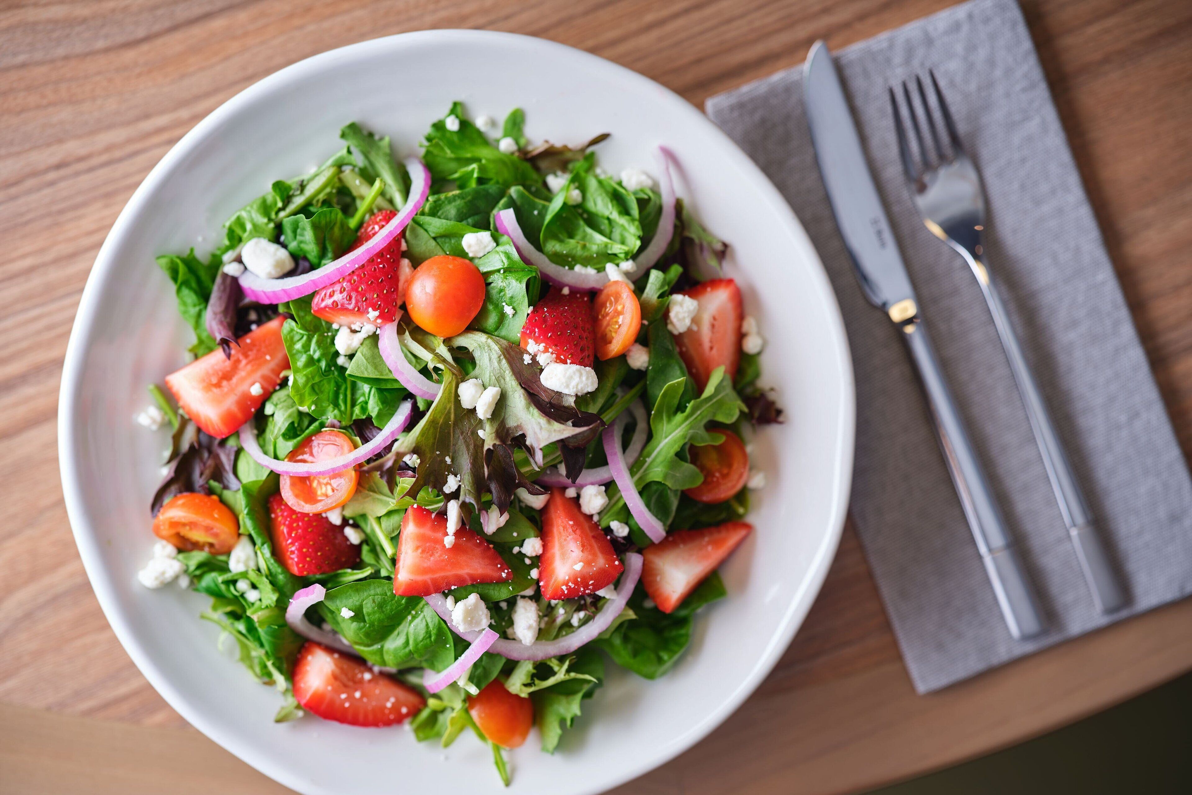 A bowl of salad with various vegetables and fruits.