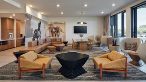 A modern living room with a sectional sofa, a black coffee table, and yellow armchairs. There is a flat-screen TV mounted on the wall, a dining area with a table and chairs, and large windows providing natural light. - Towneplace Suites By Marriott Tempe (Tempe)