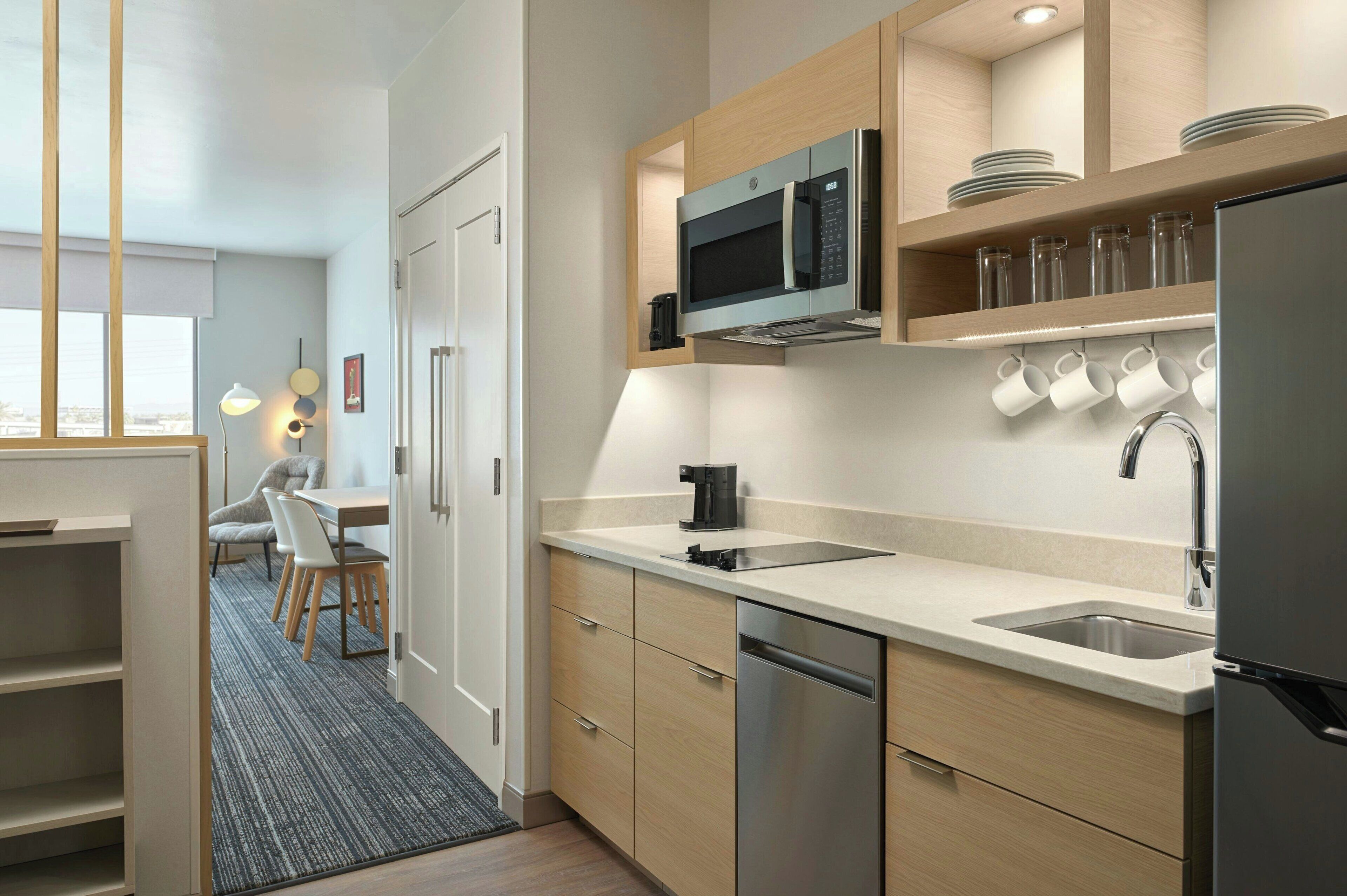 A modern kitchen with a built-in microwave, stainless steel appliances, and a sink. There is a dining area with a table and chairs visible in the background.