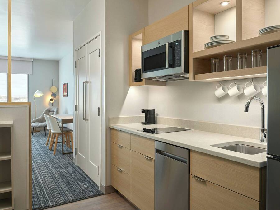 A modern kitchen with a built-in microwave, stainless steel appliances, and a sink. There is a dining area with a table and chairs visible in the background.