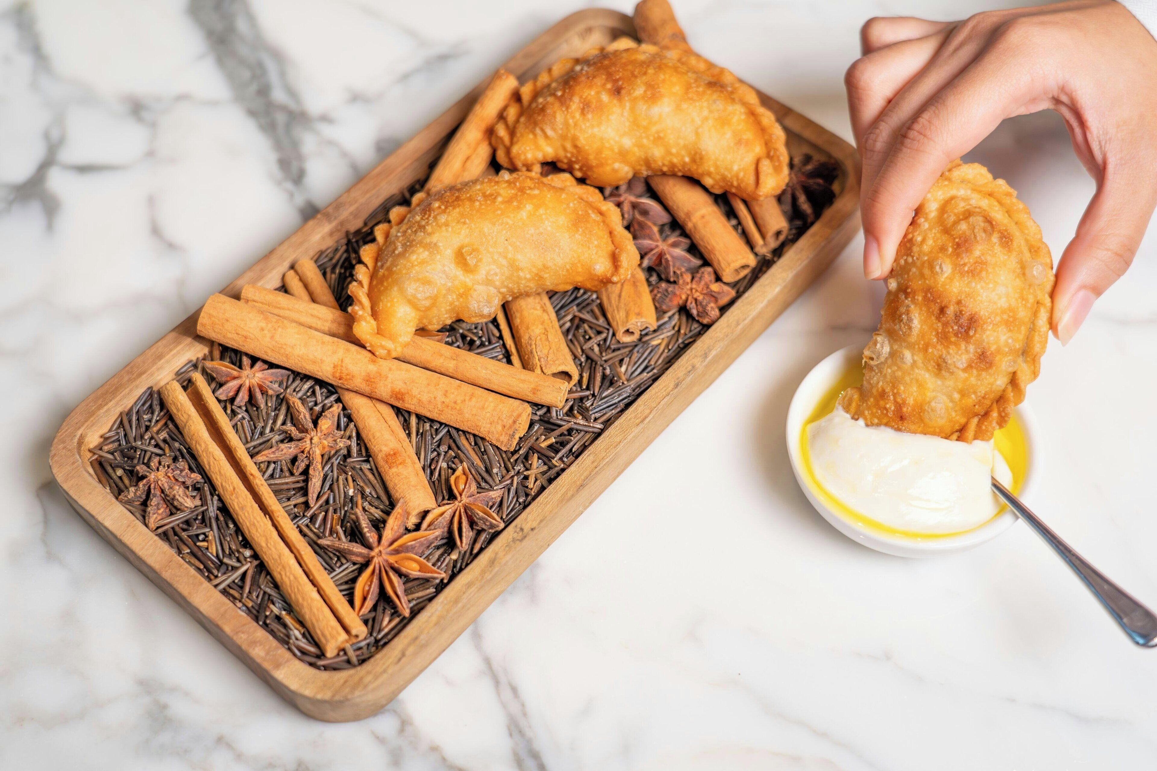 A wooden tray with fried pastries, cinnamon sticks, and star anise on a marble surface.