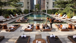 A poolside area with sun loungers, a central pool, and a massage table. - The Singapore EDITION (Singapore)