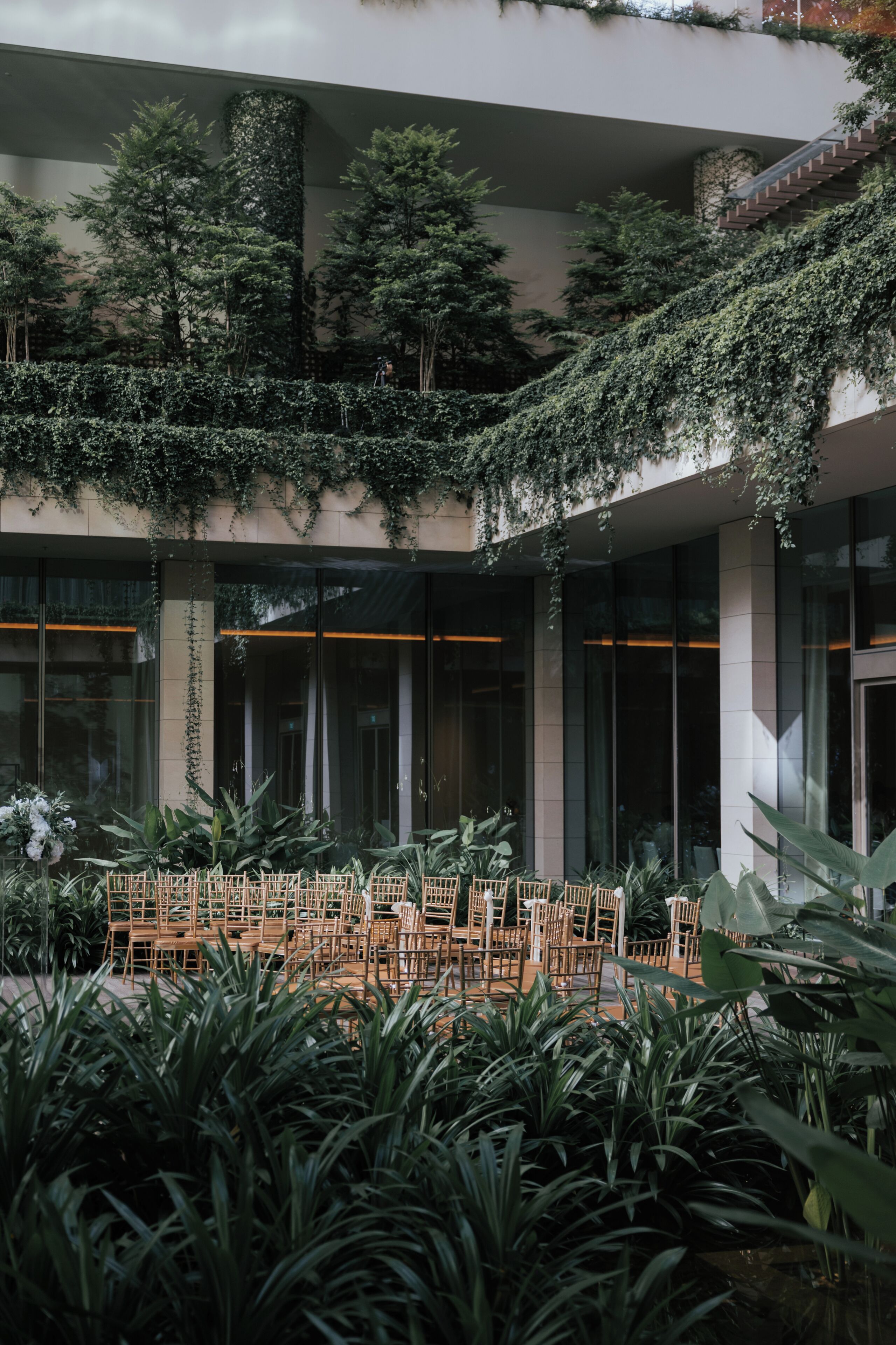A building with a covered outdoor seating area, surrounded by lush greenery and plants.