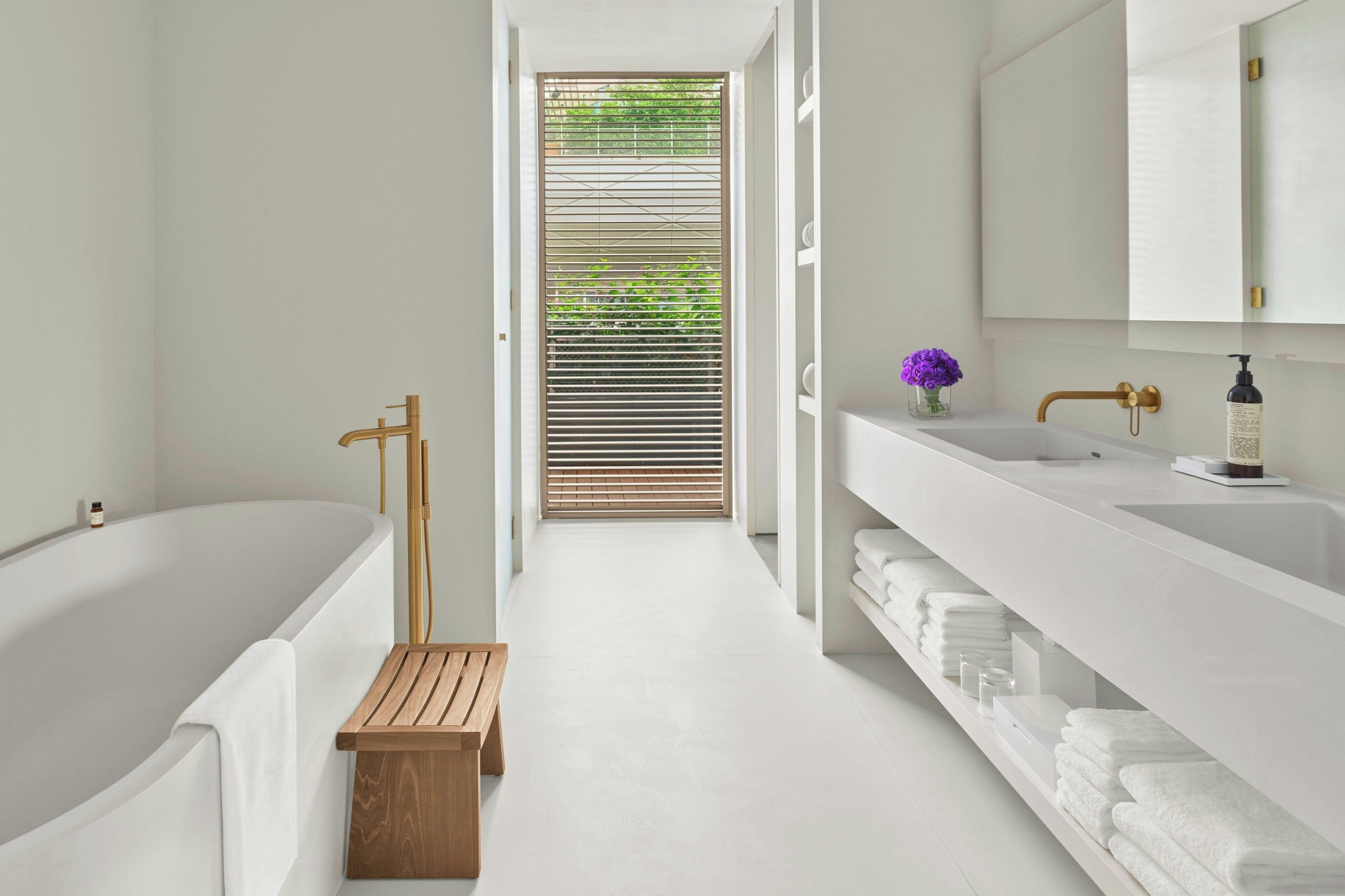 Un baño moderno con bañera, un banco de madera, un lavamanos con grifo dorado y un espejo.
