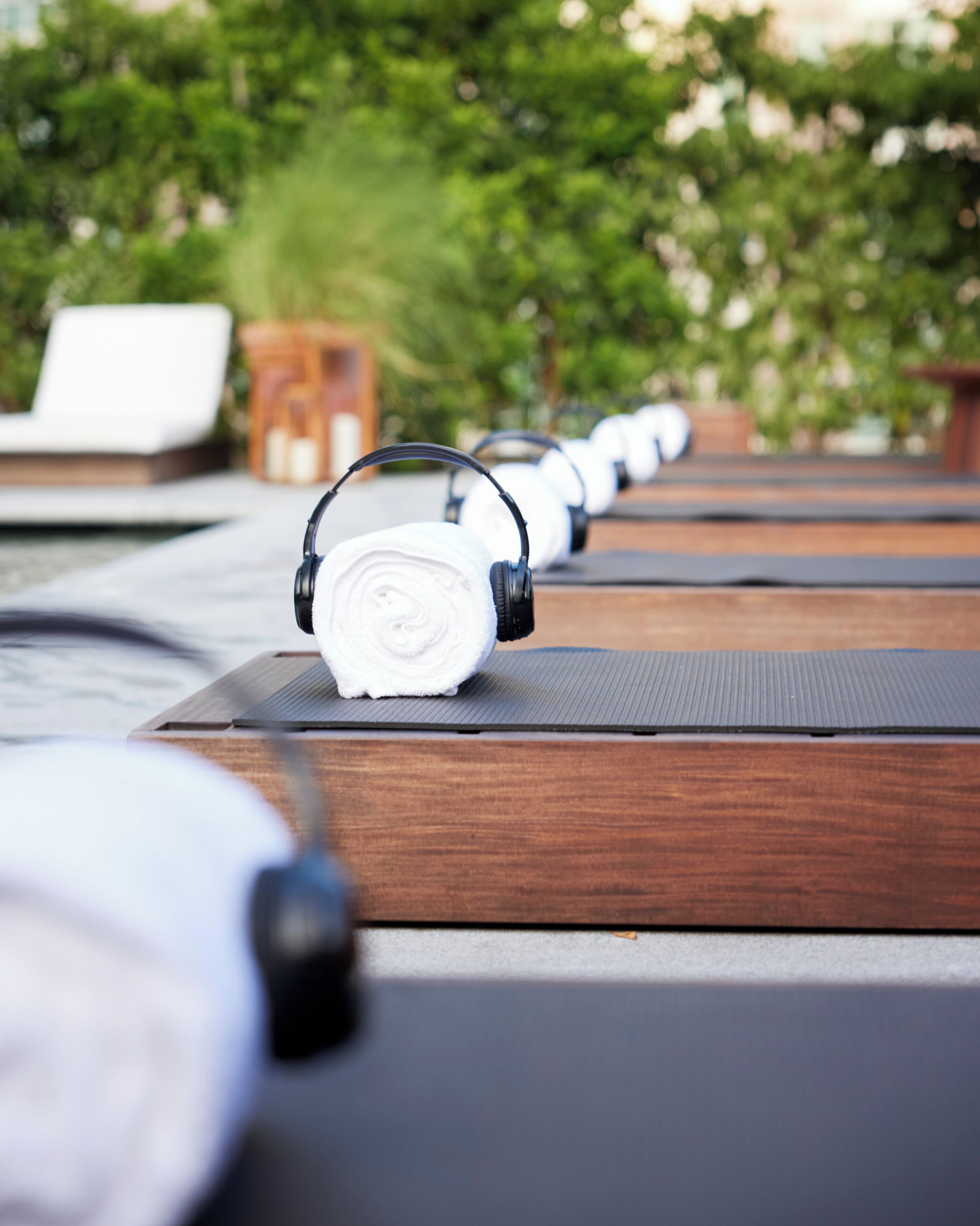 A row of yoga mats with headphones on top, arranged outdoors with a blurred green background.