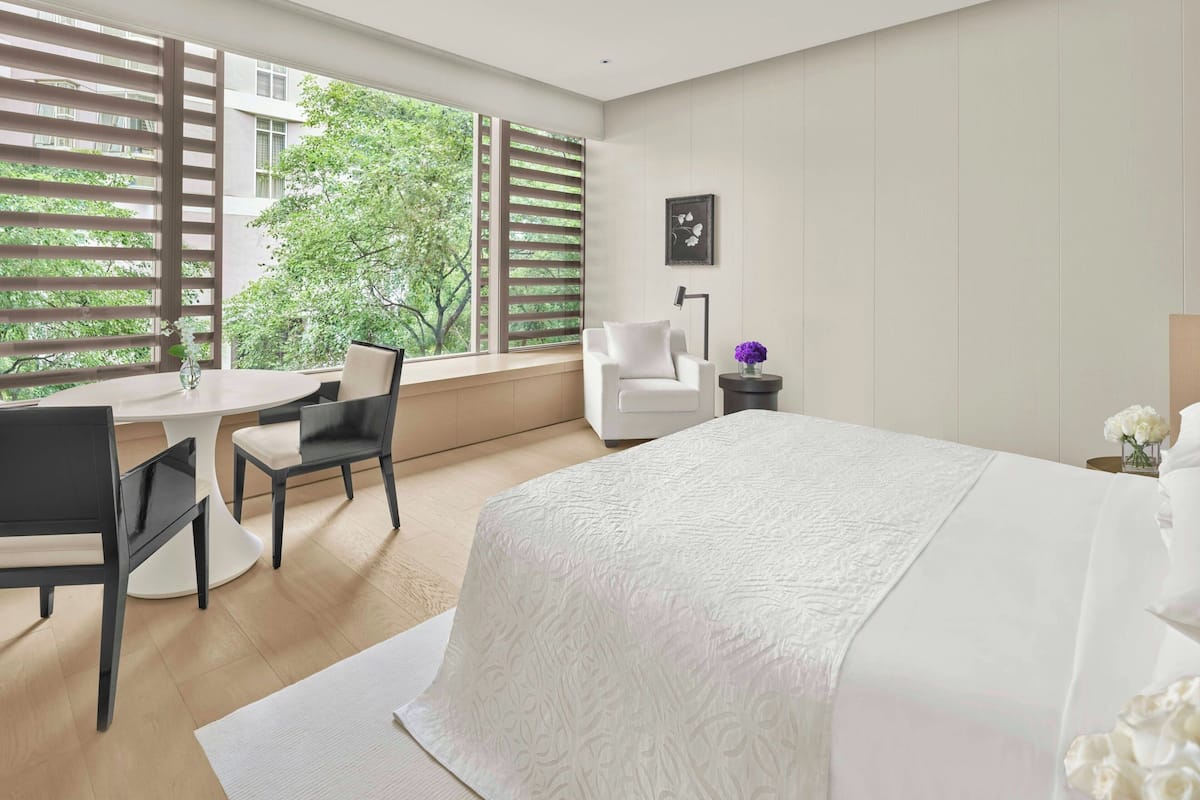 Habitación de hotel con una cama grande, un escritorio con dos sillas, una mesita y una ventana con persianas.