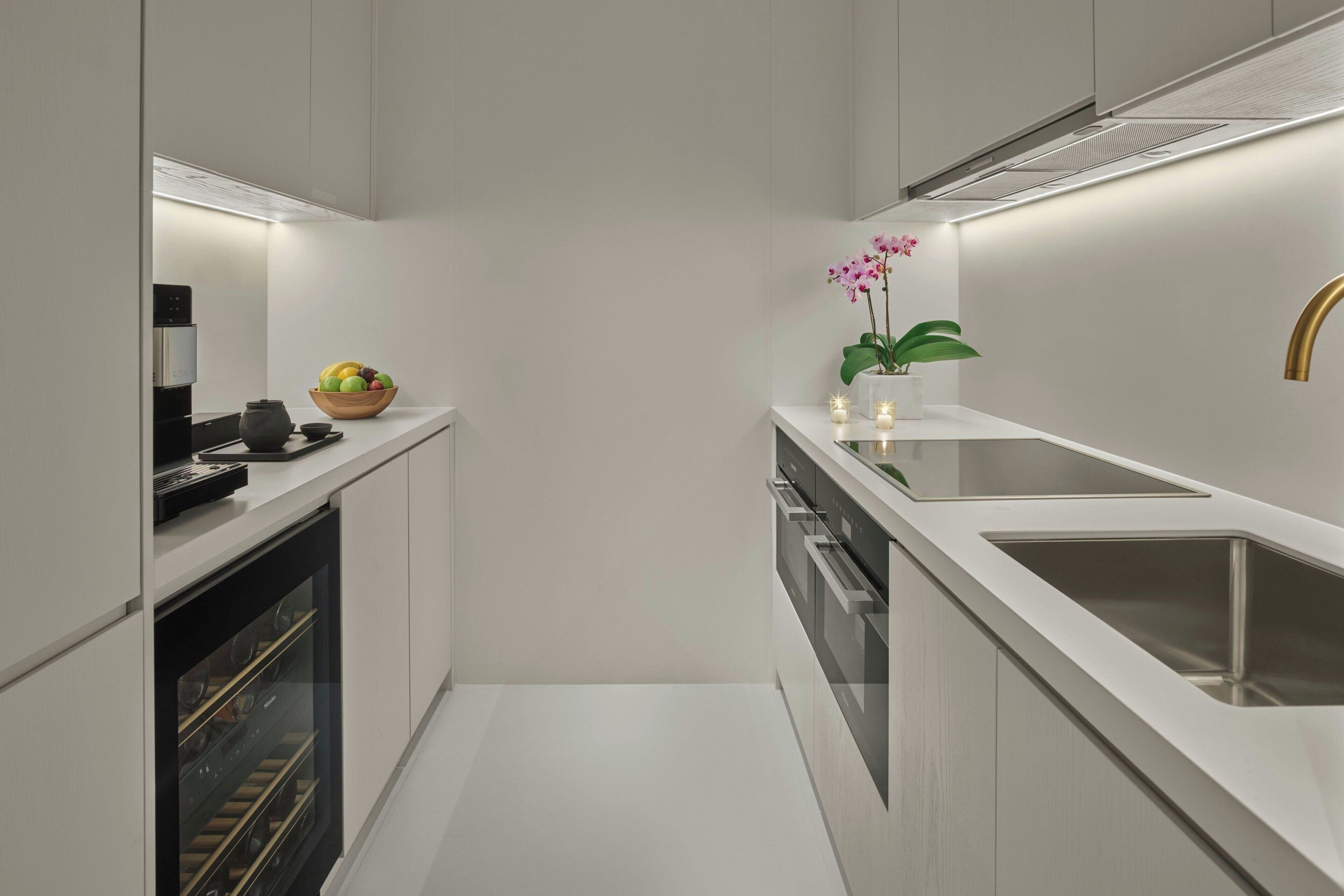 A modern kitchen with white cabinetry, a built-in oven, a sink, and a wine cooler.