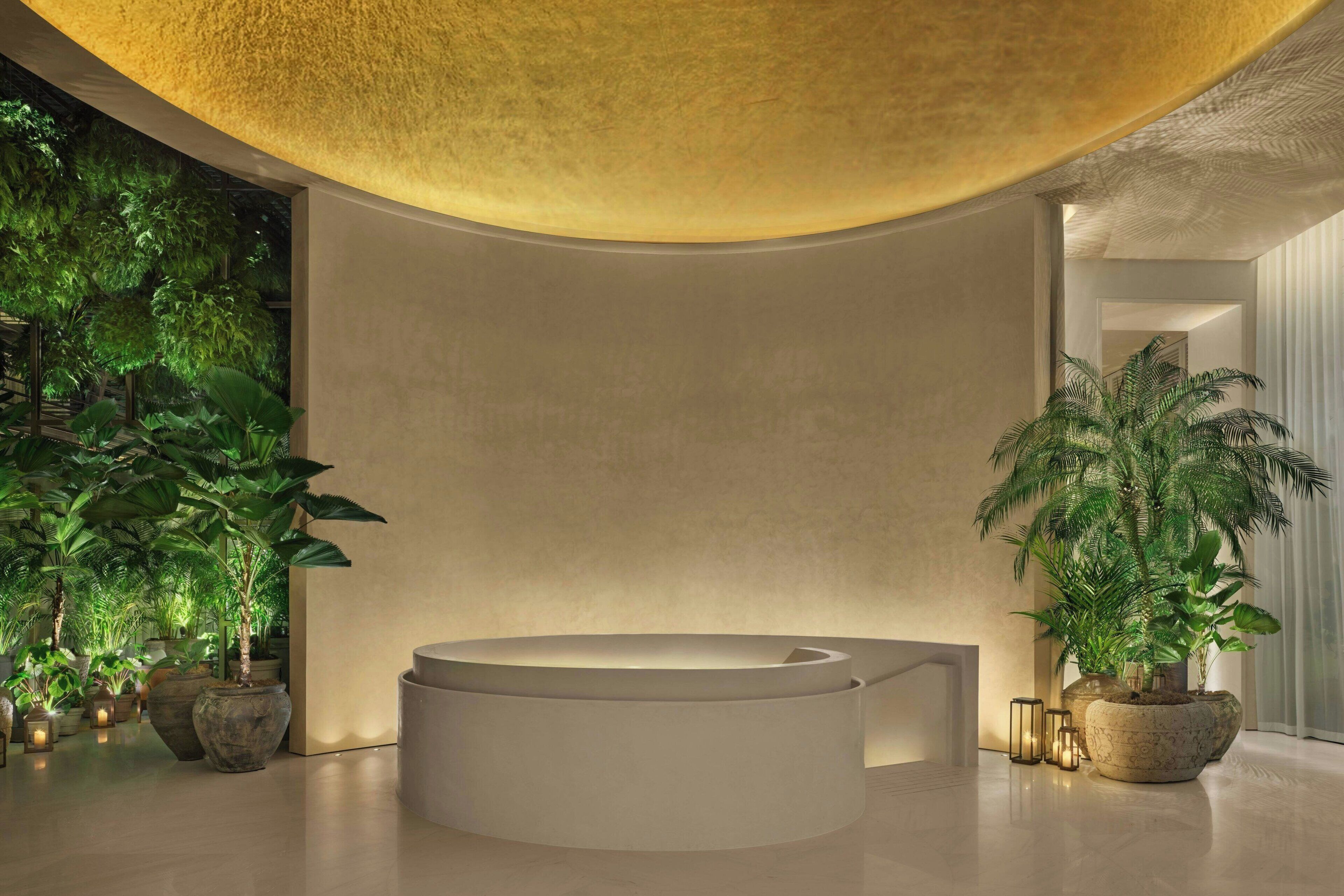 Une salle de bain moderne avec une grande baignoire, entourée de plantes en pot et agrémentée d’un plafond de forme circulaire.