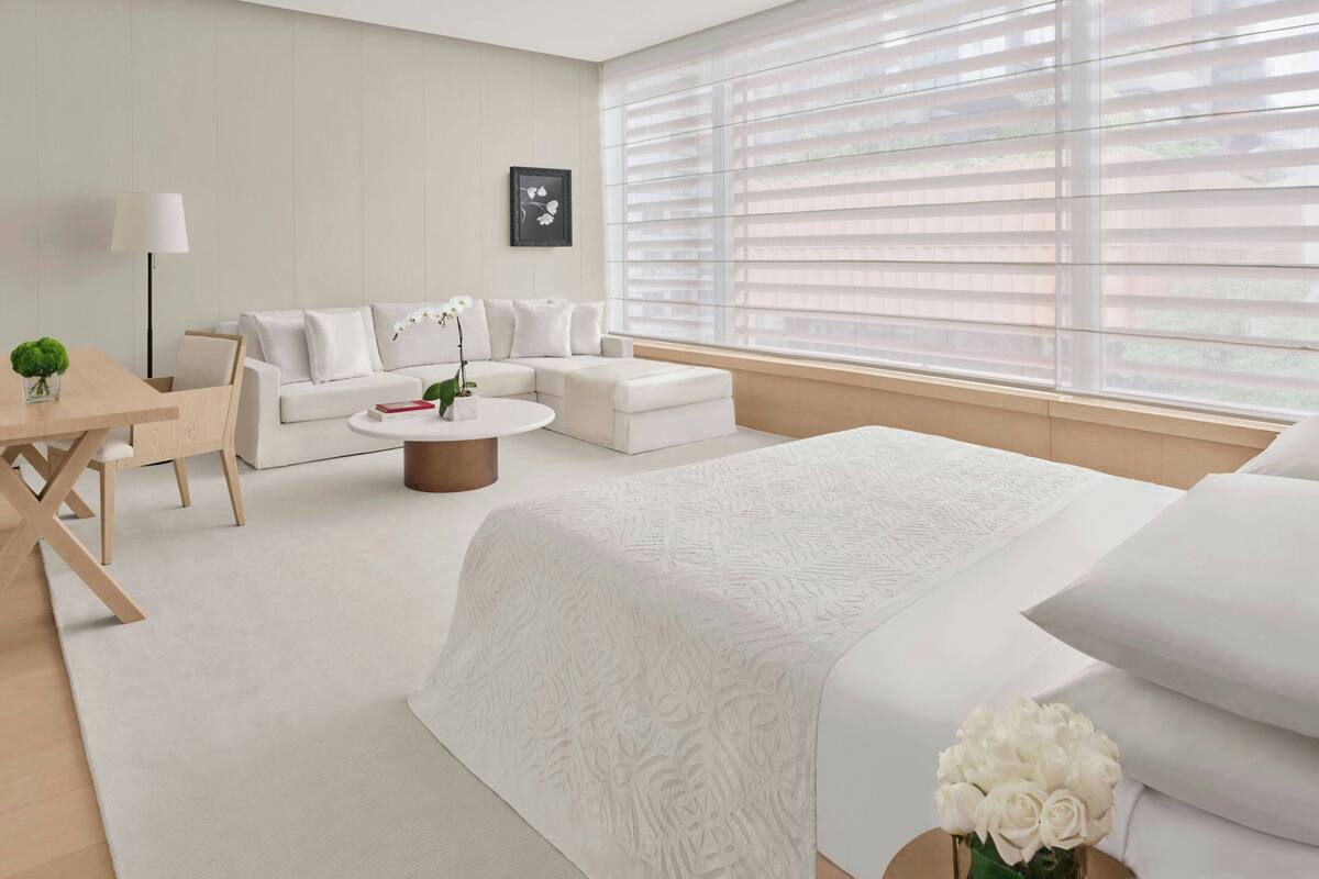 Una habitación de hotel moderna con una cama grande, un sofá blanco, una mesa de centro redonda y un escritorio con una lámpara.