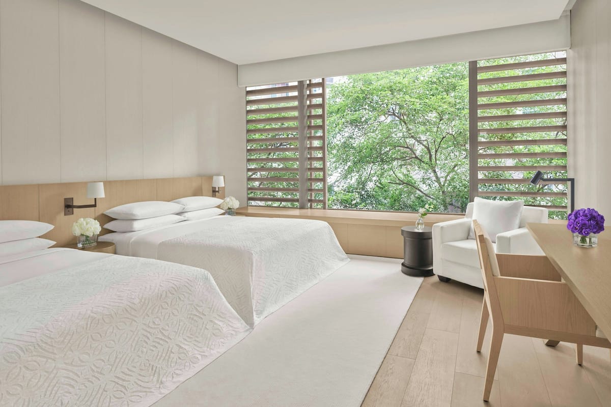 Una habitación de hotel moderna con dos camas, un escritorio de madera y ventanas grandes con persianas.