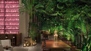 A restaurant with a long wooden table, surrounded by chairs, and a wall of green plants. - The Singapore EDITION (Singapore)