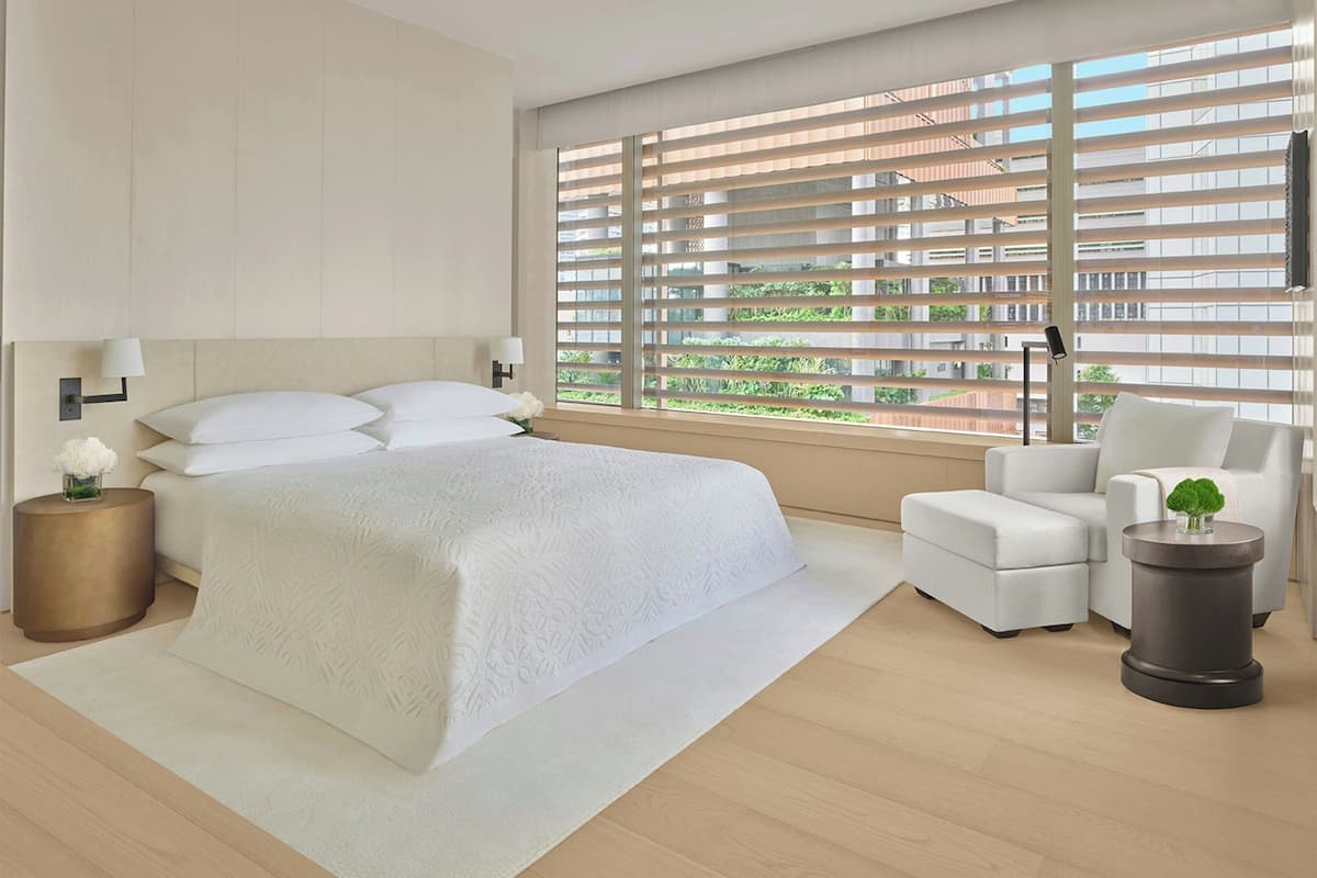 Un dormitorio moderno con una cama grande, una zona de estar con una silla, una mesita auxiliar y vistas amplias a través de grandes ventanales.