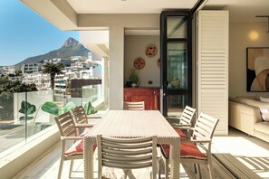 A balcony with a dining table and chairs, a kitchen area, and a view of a mountain.