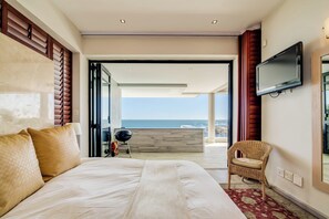 A hotel room with a large bed, a television, a wicker chair, and a view of the sea.