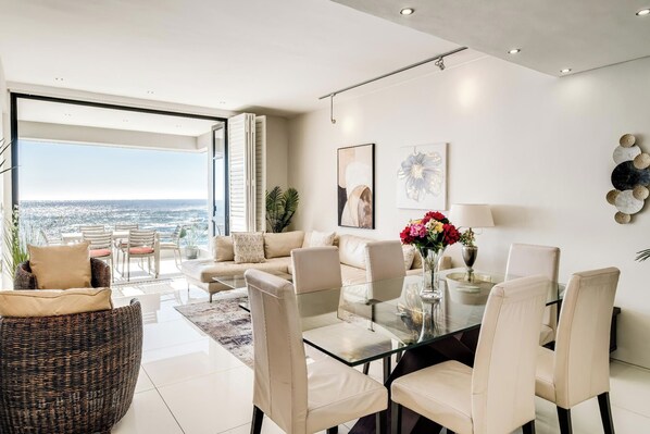 A modern living room with a glass dining table, beige sofas, and a view of the city.