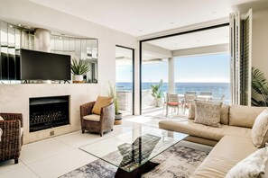 A modern living room with a fireplace, a flat-screen TV, and a glass coffee table.