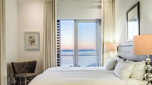 A hotel room with a large bed, a chair, a lamp, and a view of the ocean through a sliding door. - Immaculate Camps Bay Villa w Jacuzzi, Views and Pool Villa Grenache (Cape Town)
