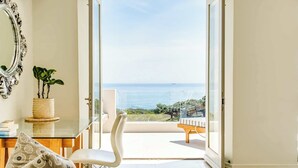 Quarto com vista para o mar, uma cadeira branca, um sofá branco e um espelho decorativo.