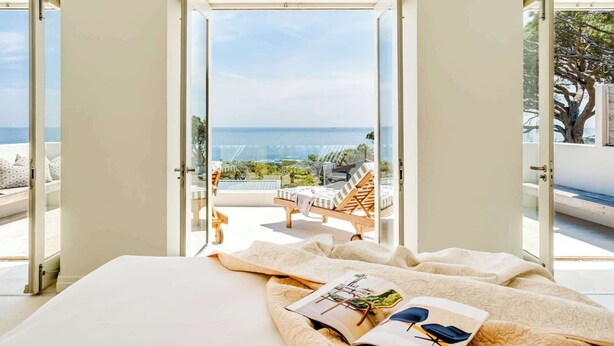 Quarto com uma grande janela, uma cama e vista para o mar.