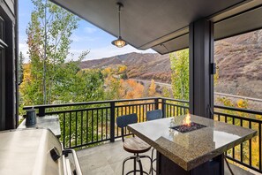 A balcony with a stone table, two chairs, and a grill with a fire. - Spacious Capitol Peak Condo at Snowmass Base Village! Balcony, Grill, Hot Tubs, Parking (Snowmass Village)
