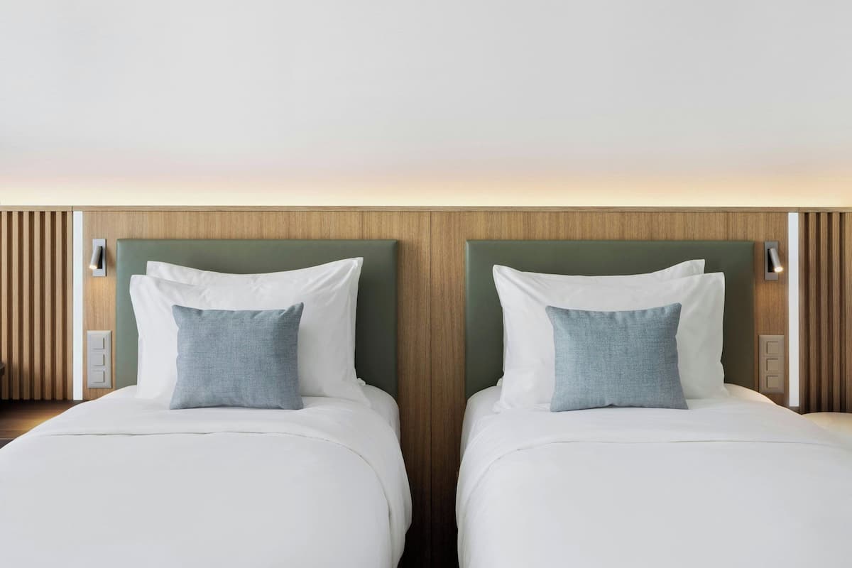 A hotel room with two beds, each with white bedding and a green headboard.