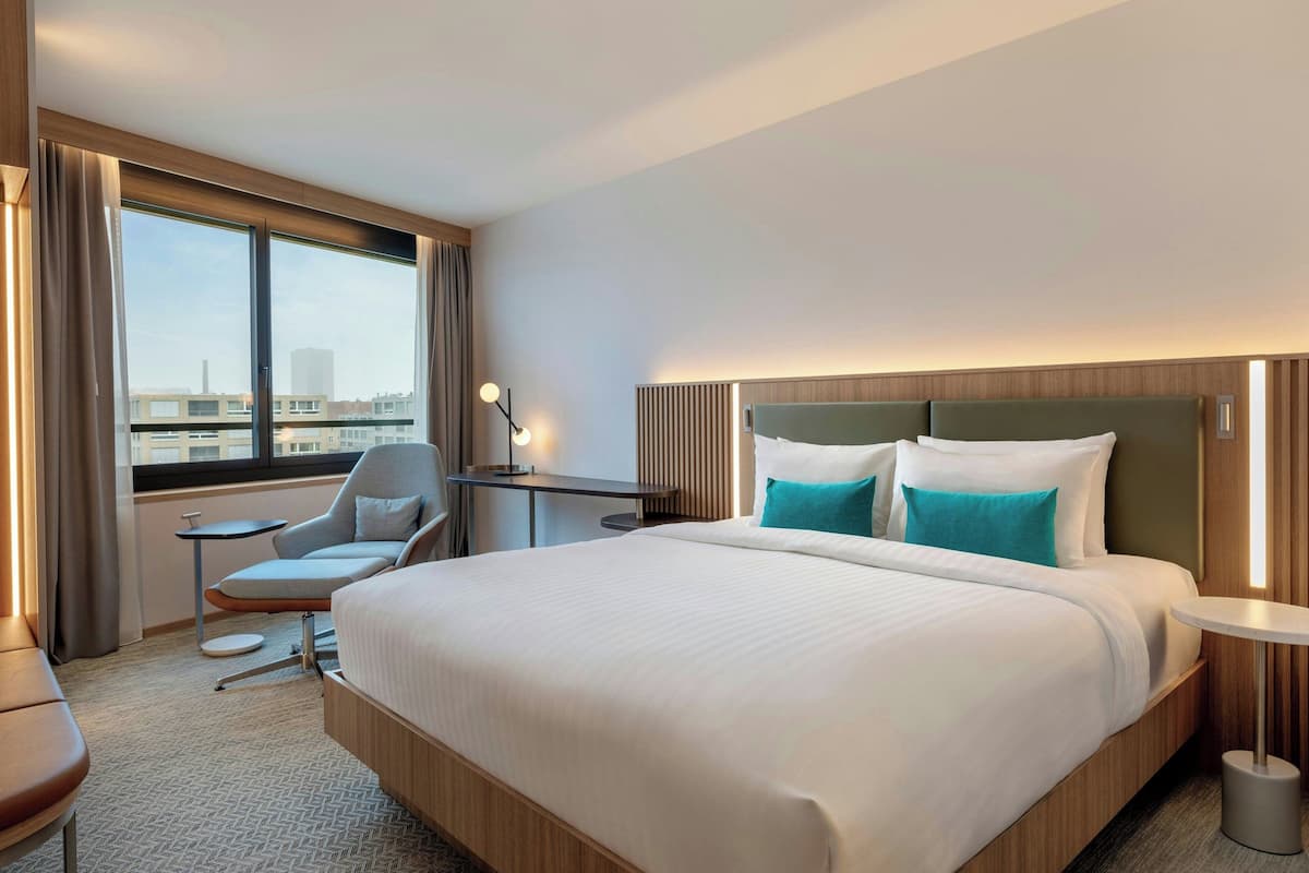 A hotel room with a large bed, a desk, a chair, and a window with curtains.