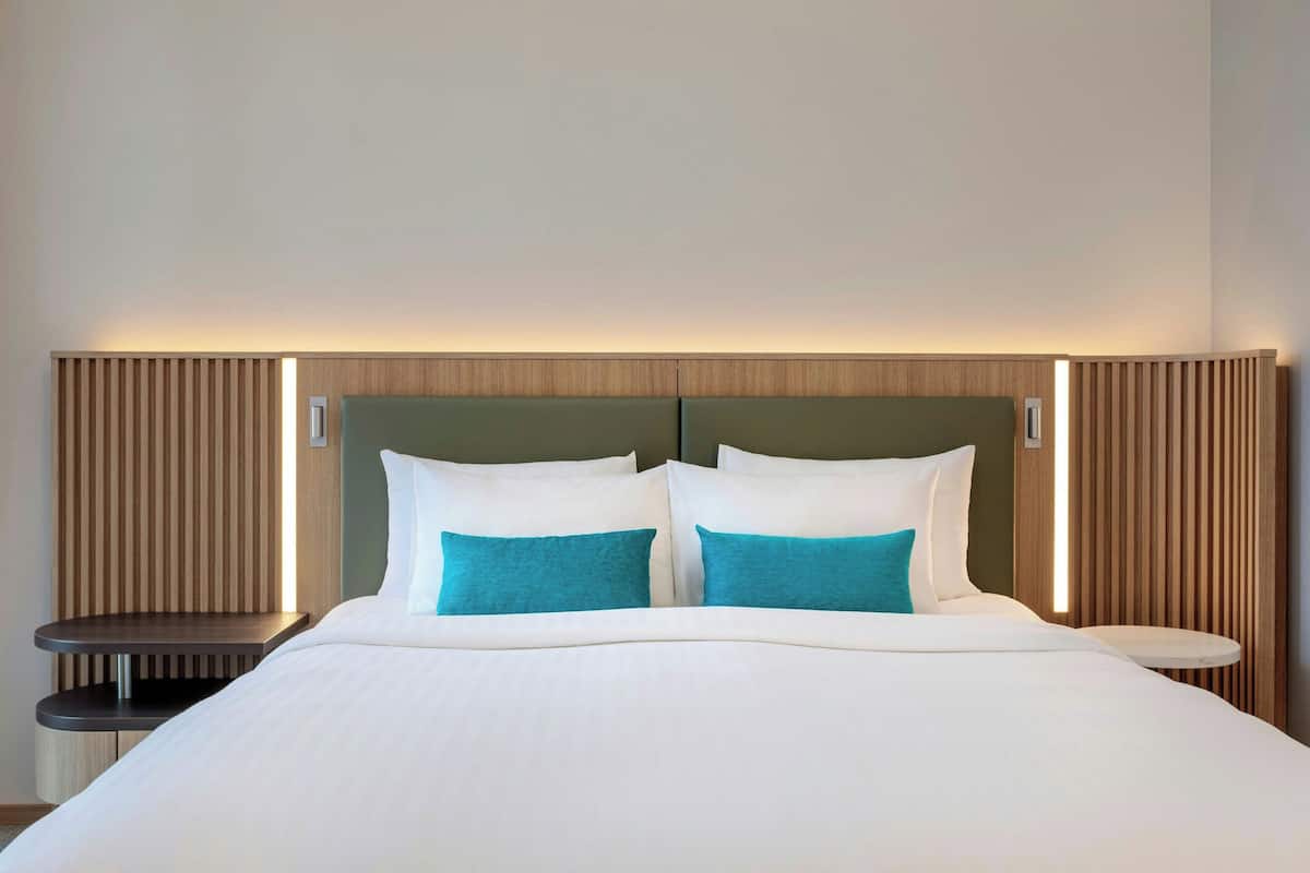 A neatly made bed with white linens and two teal pillows, flanked by wooden headboards and bedside tables.