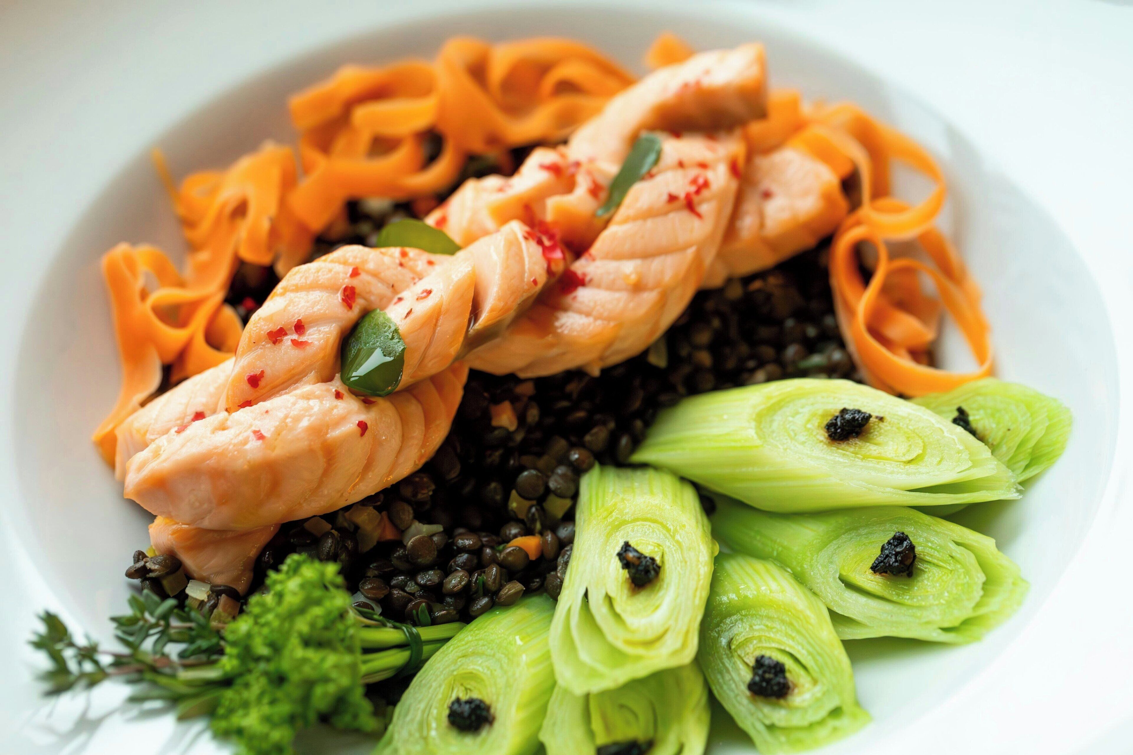 Une assiette de nourriture comprenant du saumon, des pâtes et des légumes.