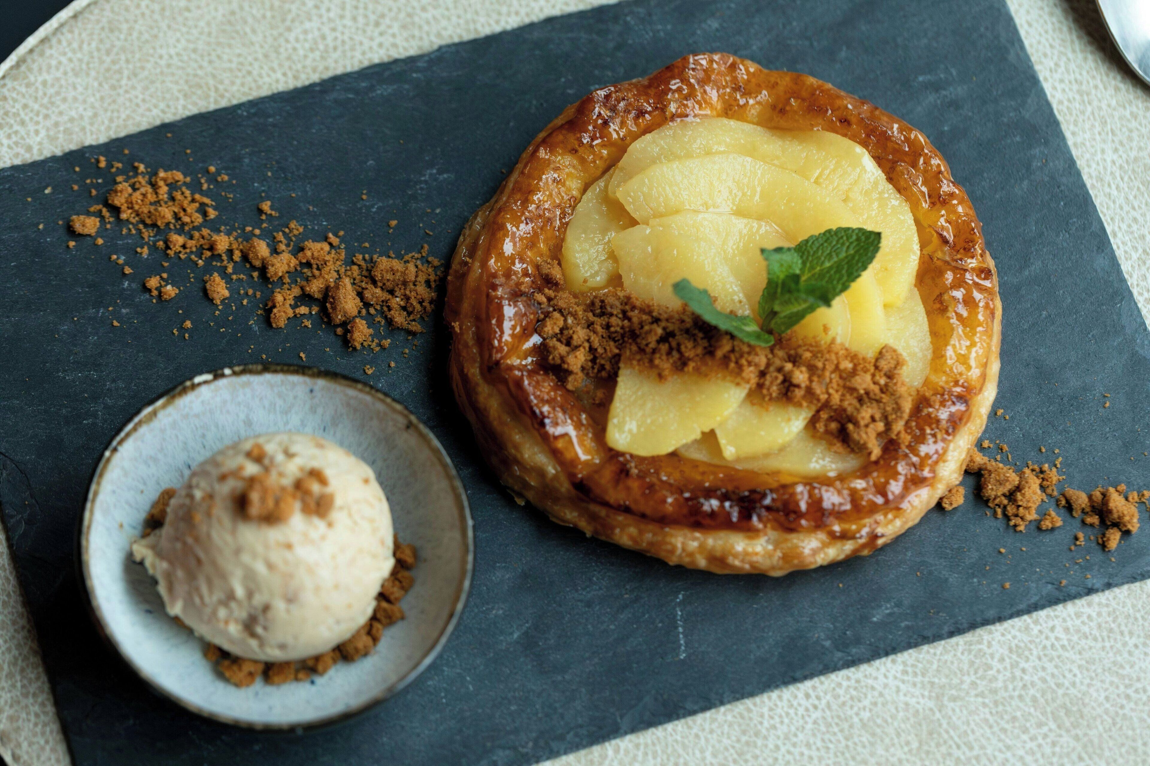 Un dessert avec une croûte caramélisée, une feuille de menthe en décoration et une boule de glace servie sur une assiette en ardoise.