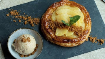 Un dessert avec une croûte caramélisée, une feuille de menthe en décoration et une boule de glace servie sur une assiette en ardoise.