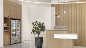 Un área de recepción moderna con un mostrador de madera, una planta en maceta, un refrigerador con bebidas y una pared de paneles de madera.